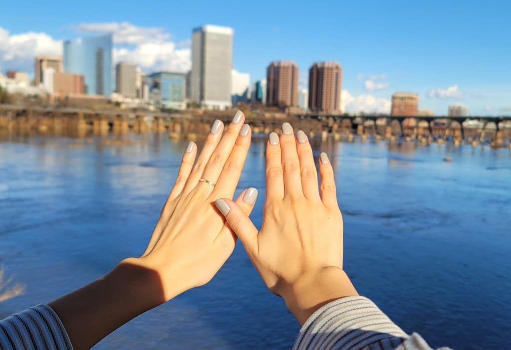 Manicured hands raised against a river and city skyline