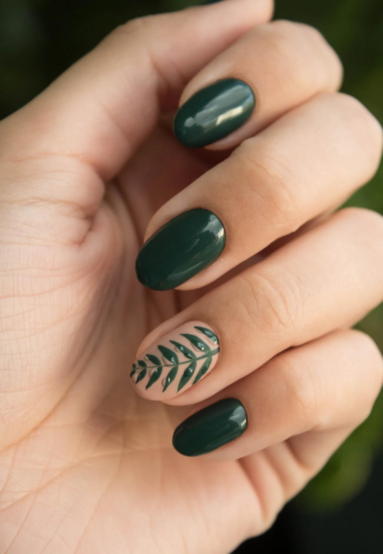 Deep green botanical nail art on a manicured hand