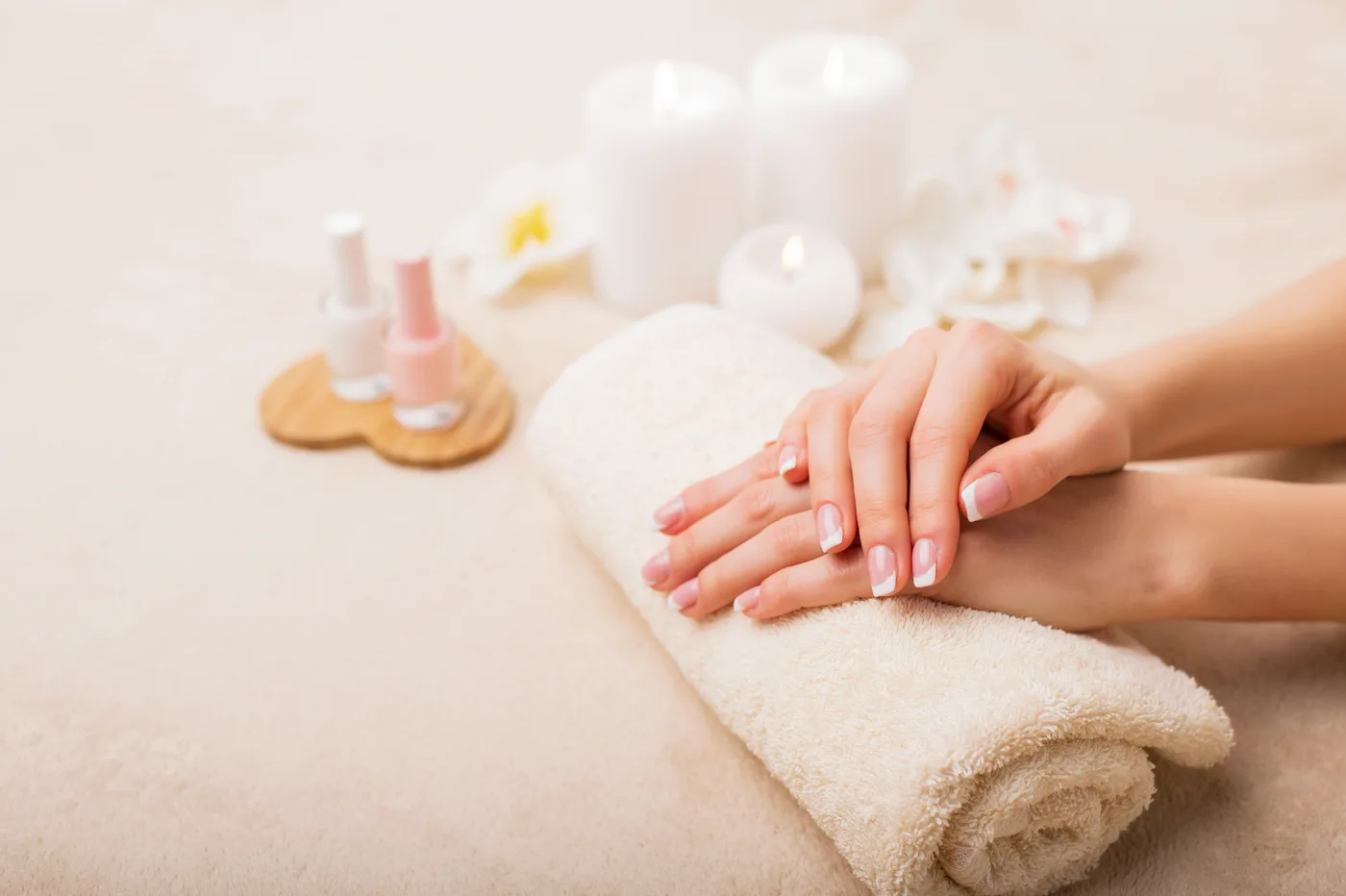 French manicured hands resting on a spa towel with candles